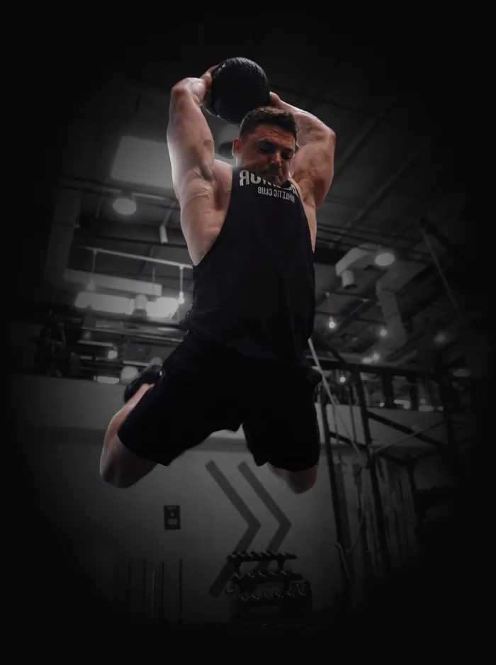 Ivan slamming a medicine ball overhead mid-jump in the gym