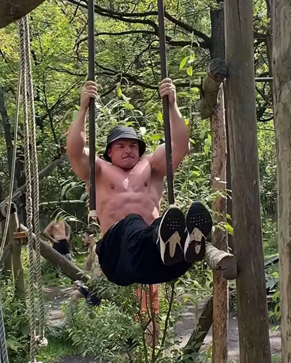 Ivan holding an L-sit on suspension bars in a summer forest